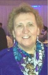 Linda, our Founder and Executive Director, wears a big smile, a purple top, and a lightweight scarf that resembles stained glass.